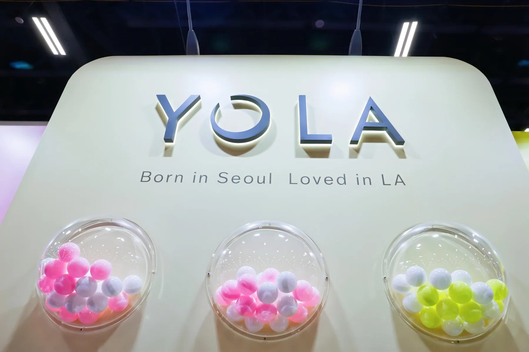 The Yola booth signature: 'Born in Seoul. Loved in LA.' above a row of colorful display domes.